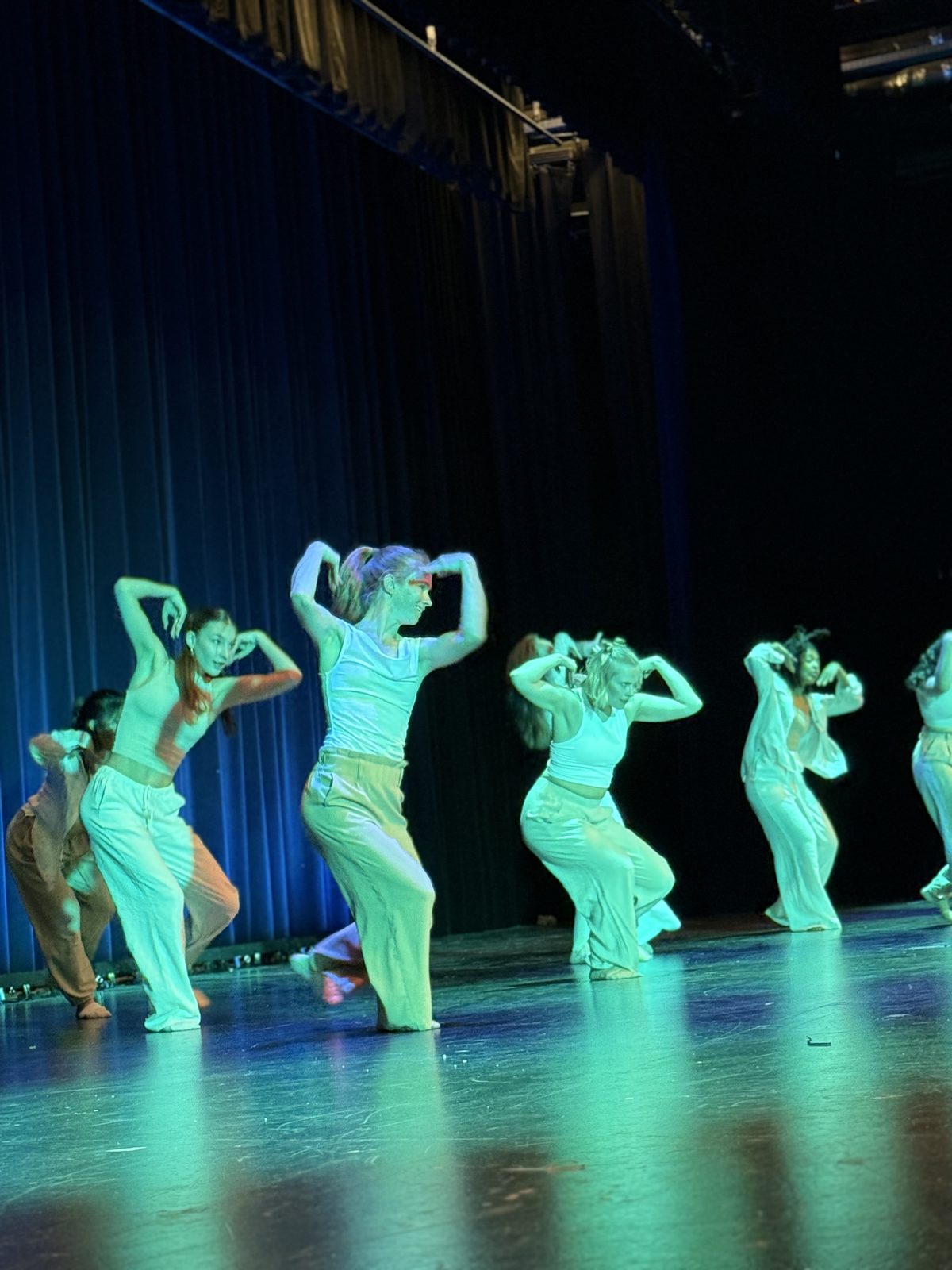 Tanzgruppe in Weiß in türkisfarbenem Licht, mitten in der Choreografie